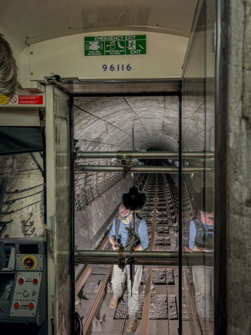 View from inside the driver's cab on a London tube (not moving) - door is open and specialist camera rig and 360 video camera can be seen mounted to the fron of the train. Cameraman visible on tracks in front of the train.