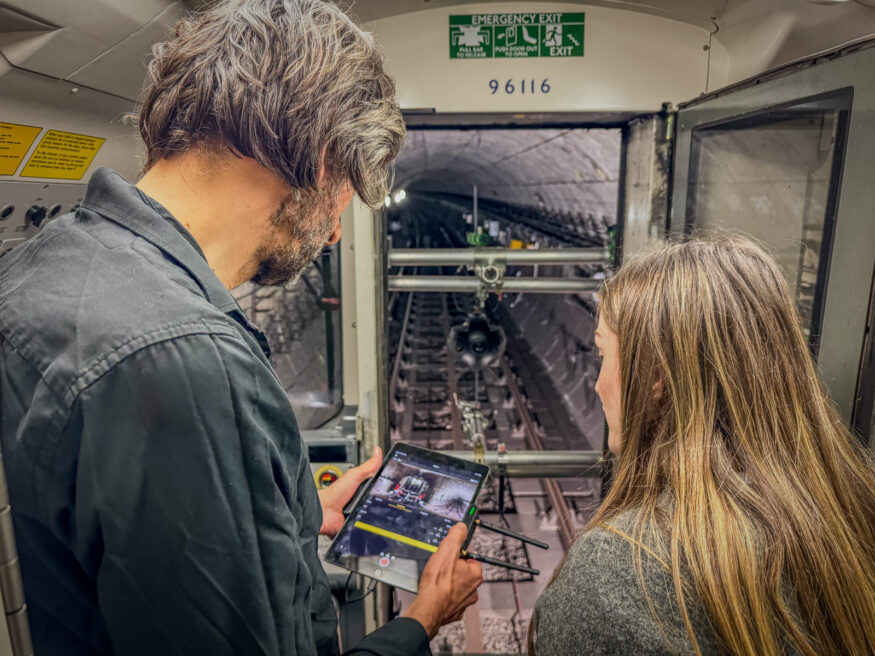 Image shows a 360 video cameraman and client checking the 360 video footage on an ipad, while on a shoot in the driver's cab of a london tube train.