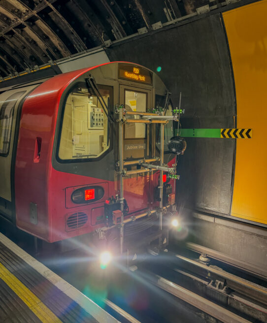 Image shows the front of a London underground train on a station. The train has specialist rigging on the front to hold the 360 video camera.