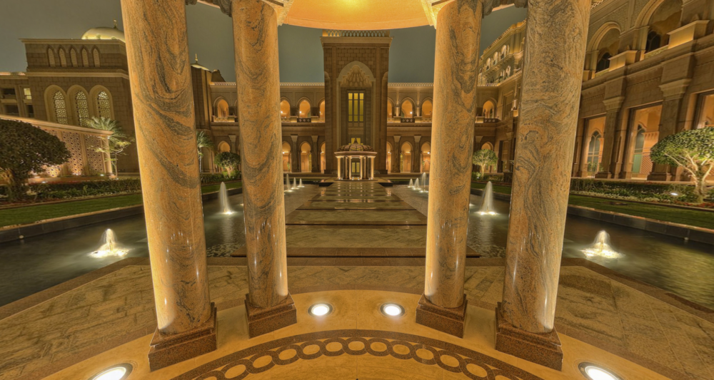 The most expensive hotel in the world - Emirates Palace, Abu Dhabi. View taken from the virtual tour looking out from under a columned folly along a path towards the hotel. The path is flanked by an ornamental lake. It is night and the fountains are lit.